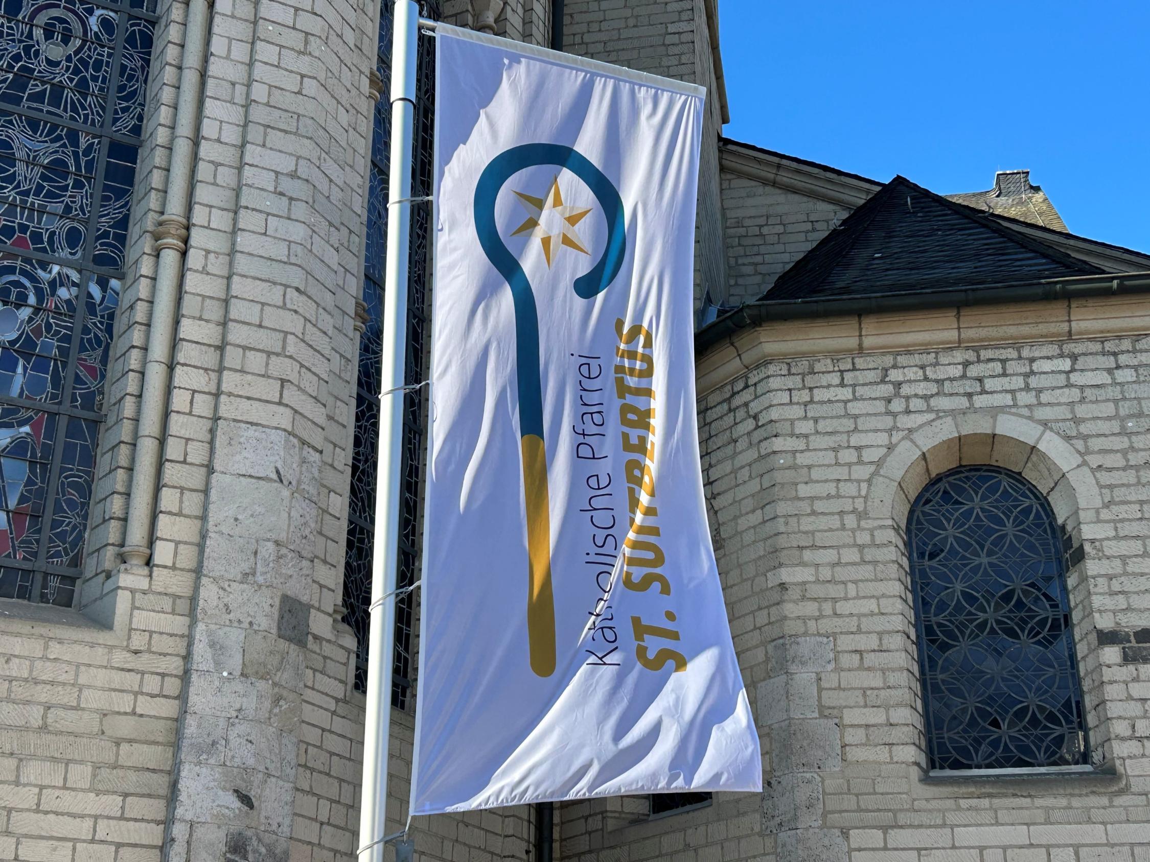 Die Flagge der Pfarrei St. Suitbertus mit dem neuen Logo vor der Basilika St. Suitbertus in Kaiserswerth