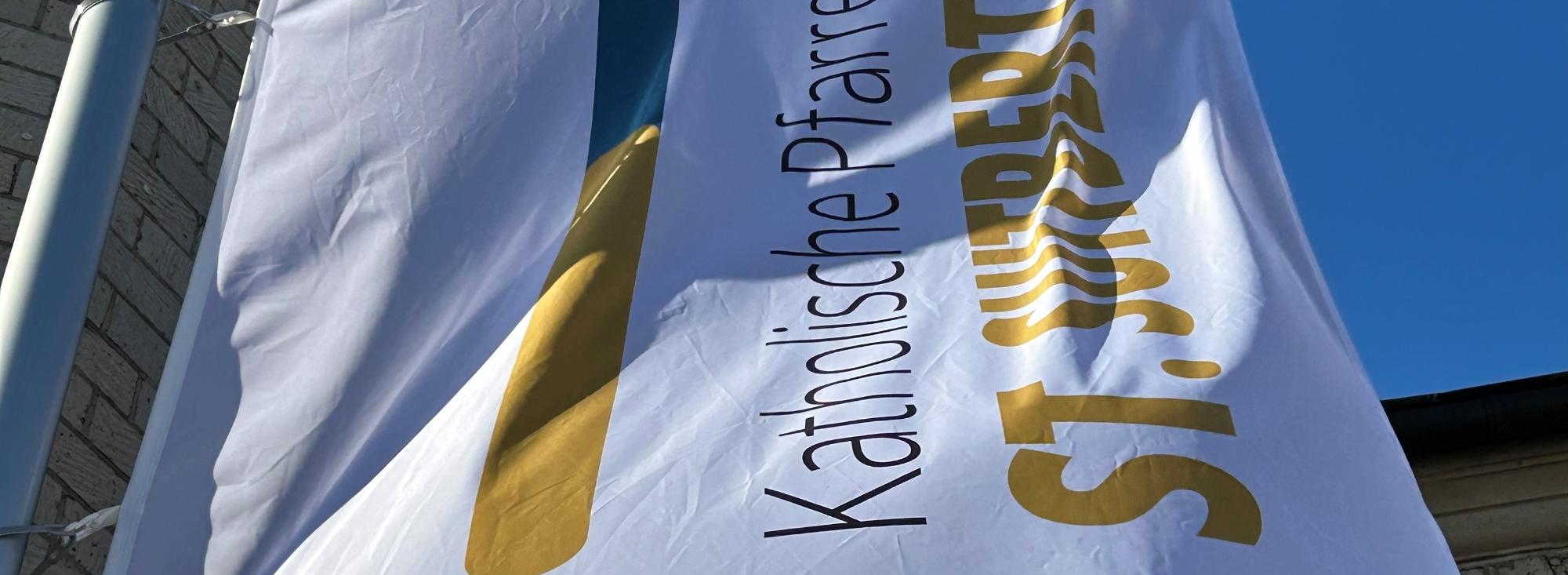 Die Flagge der Pfarrei St. Suitbertus mit dem neuen Logo vor der Basilika St. Suitbertus in Kaiserswerth