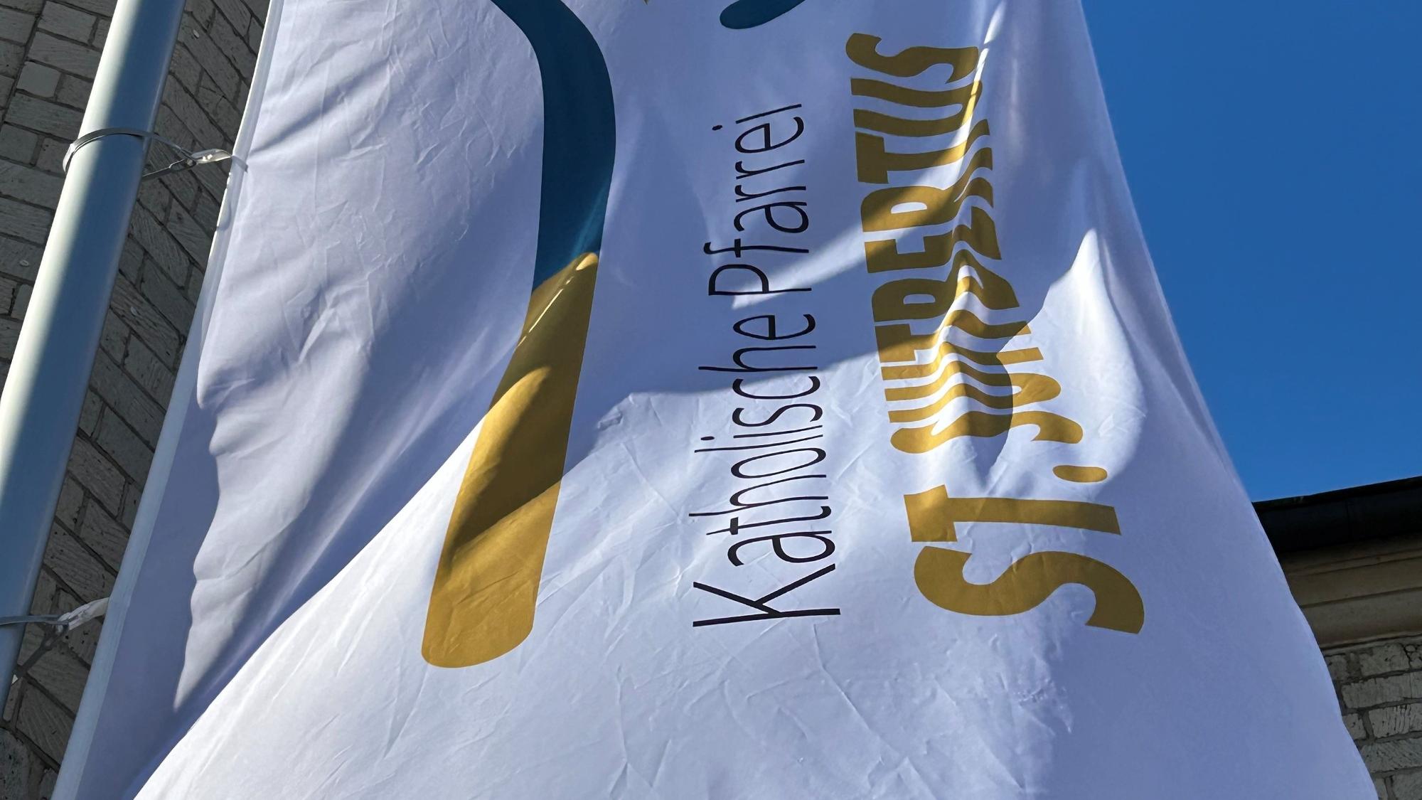 Die Flagge der Pfarrei St. Suitbertus mit dem neuen Logo vor der Basilika St. Suitbertus in Kaiserswerth