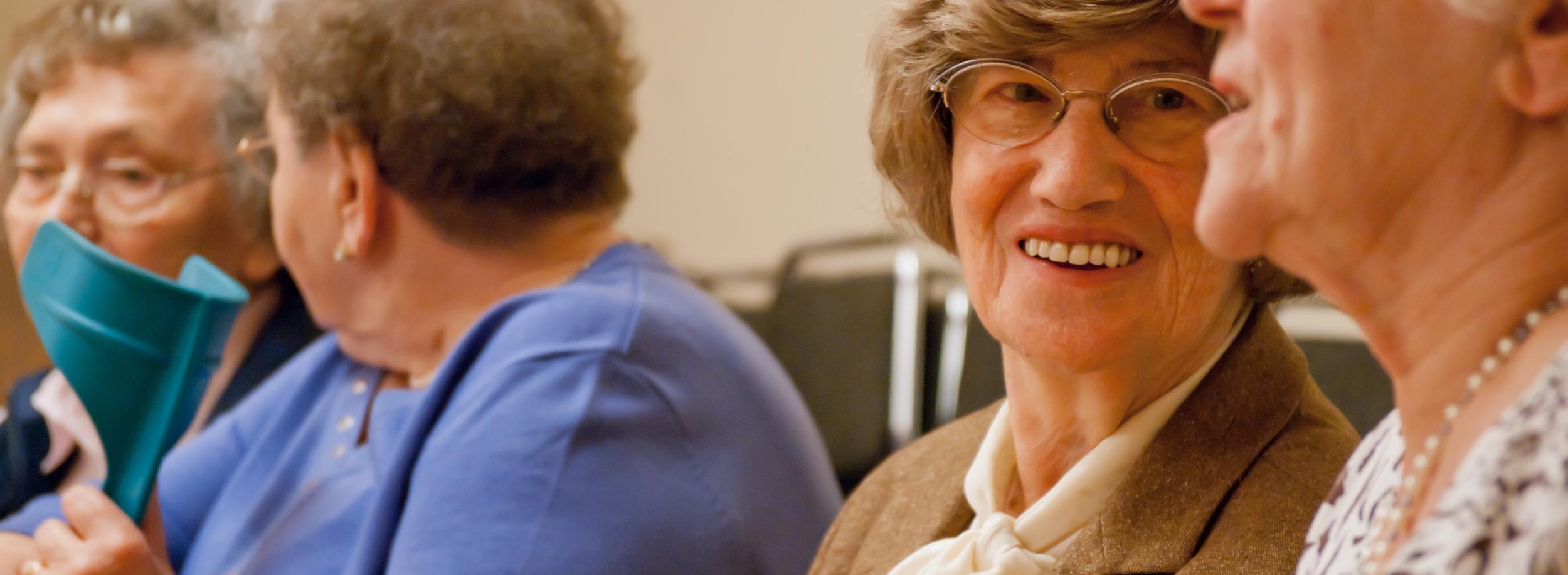 Sie sehen 4 Seniorinnen nebeneinandersizen und fröhlich im Gespräch