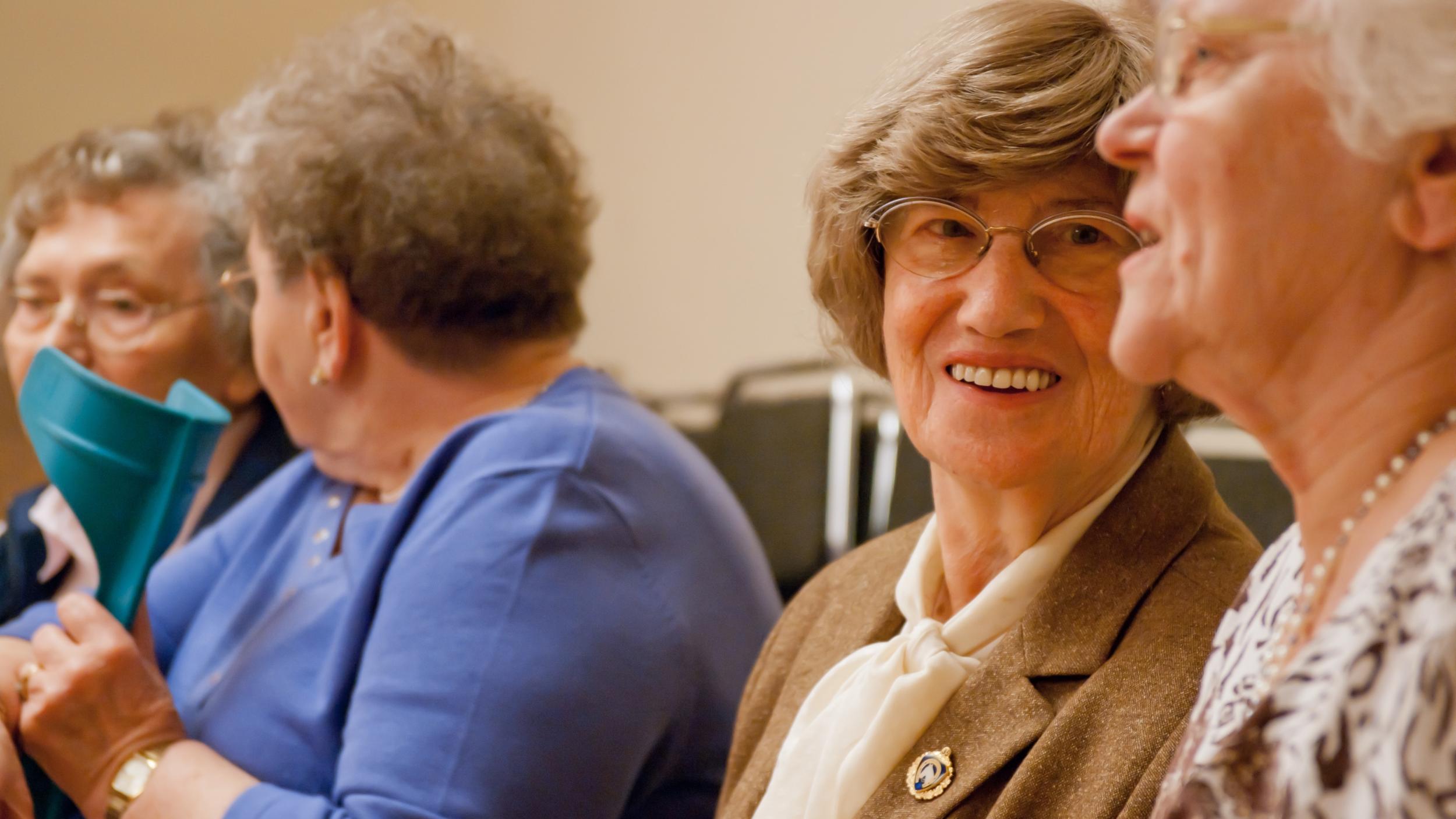 Sie sehen 4 Seniorinnen nebeneinandersizen und fröhlich im Gespräch